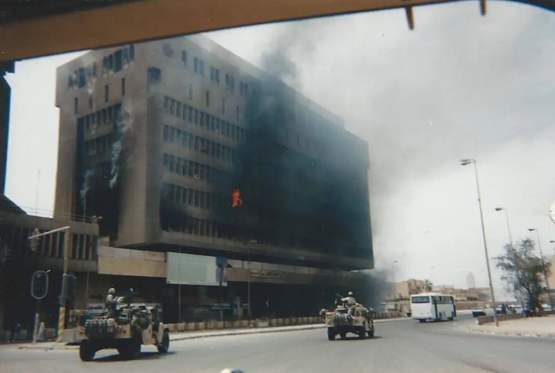 Building on fire with military vehicles nearby.