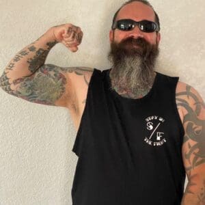 Bearded man flexing arm with tattoos and sunglasses.