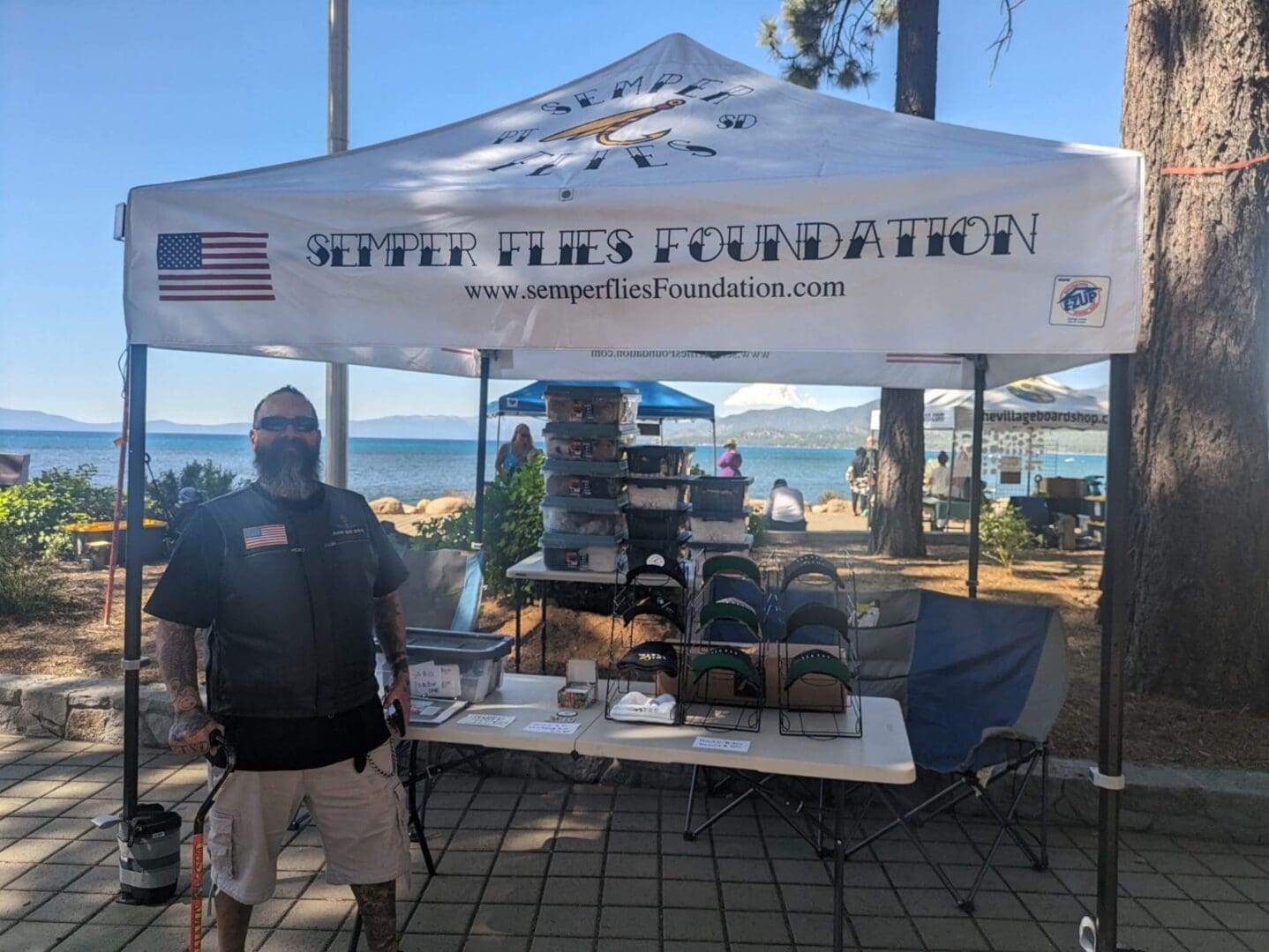Man at Semper Flies Foundation booth, outdoors.