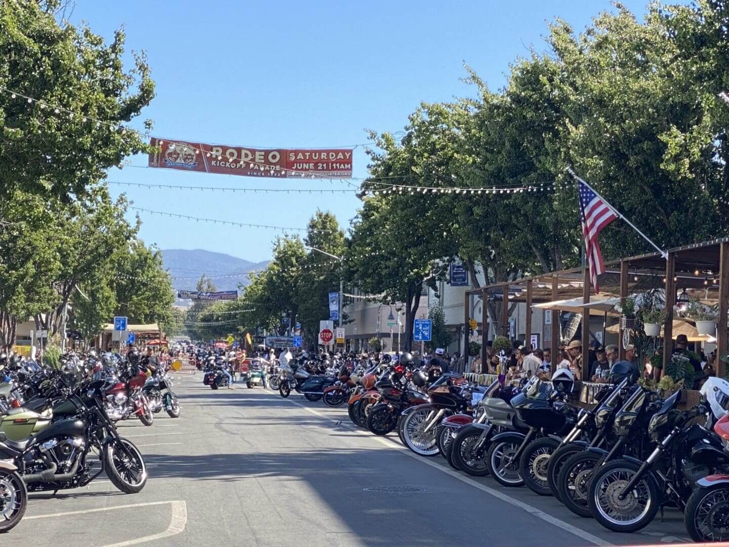 Street filled with parked motorcycles, event banner.