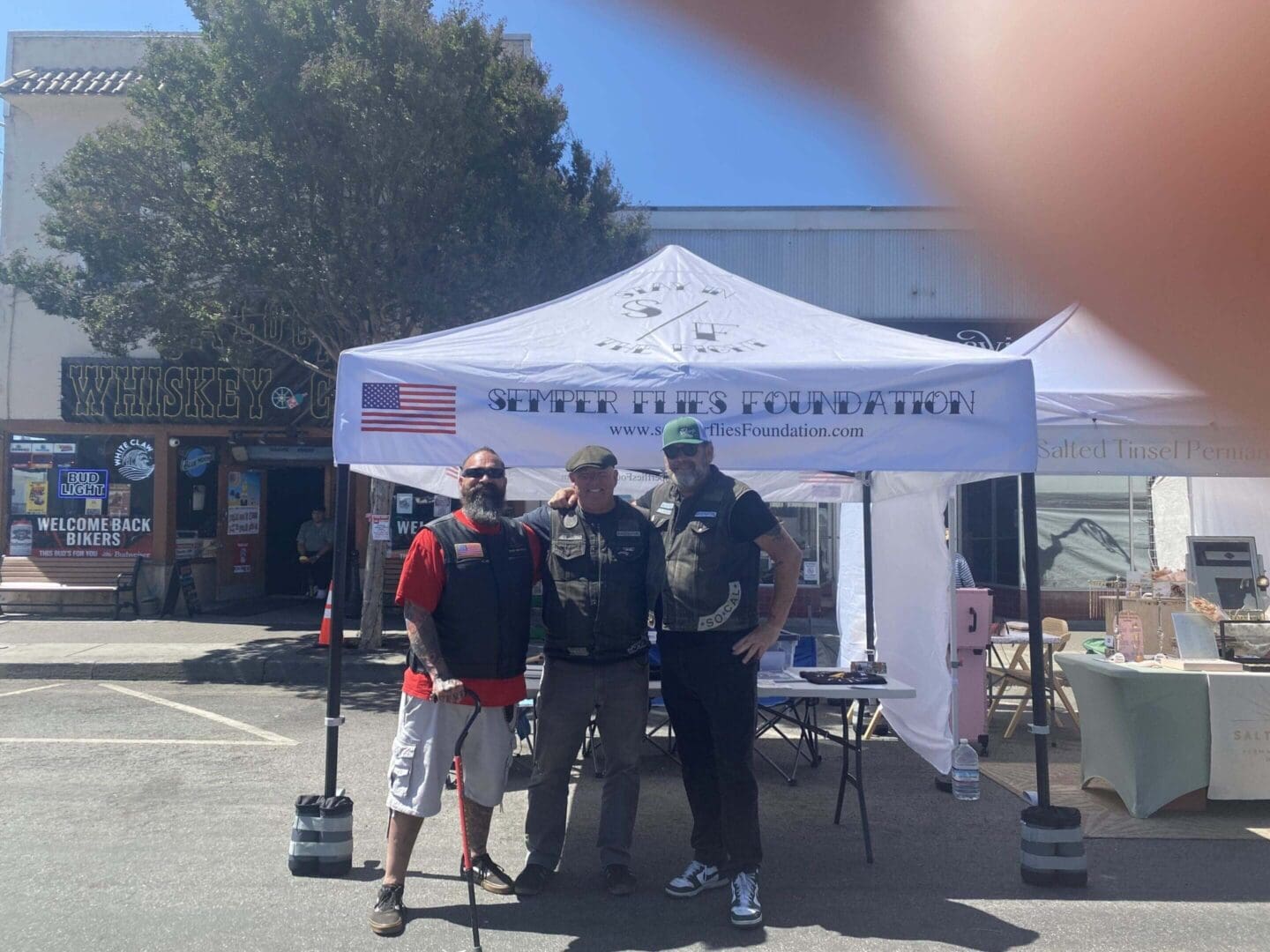 Three people standing under a canopy tent.